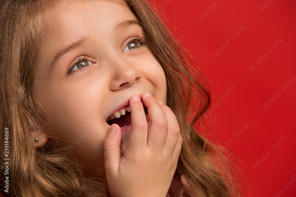 The happy teen girl standing and smiling against red background.