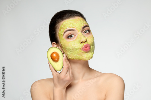 Beautiful young woman with facial mask and fresh avocado on light background photo