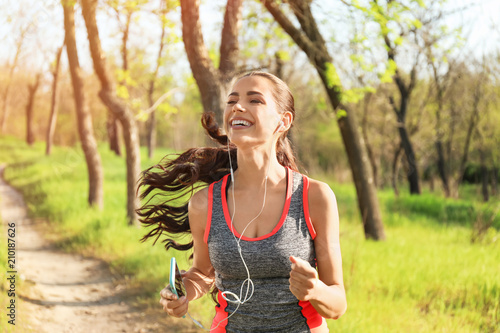 Sporty young woman listening to music while running in park