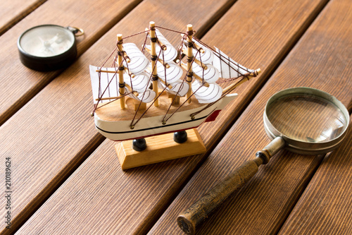 Model of old sailboat, old magnifying glass and compass on wooden background. Travel concept