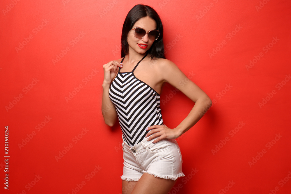 Beautiful young woman in swimming suit and shorts on color background Beautiful young woman in swimming suit and shorts on color background