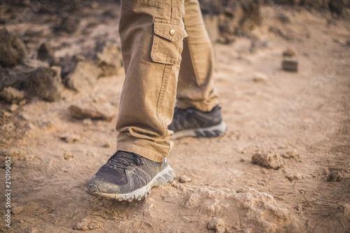 closeup of shoes do trekking on the ground in desertic arid place. man freedom concept and dirty of sand wear. exploring and discover alternative vacation and places around the world