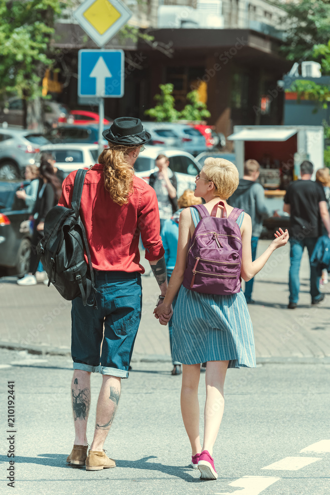 back view of young couple with backpacks walking in city back view of young couple with backpacks walking in city