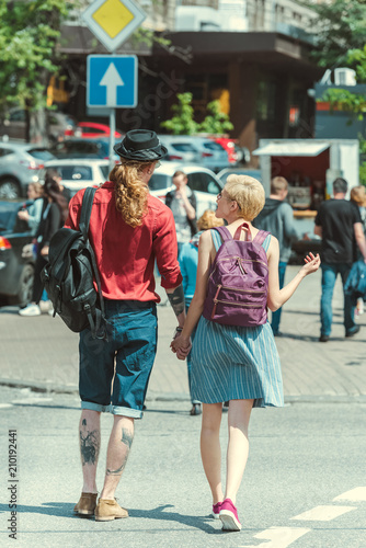 back view of young couple with backpacks walking in city