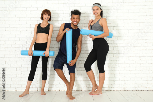 Group of sporty people with yoga mats near white brick wall