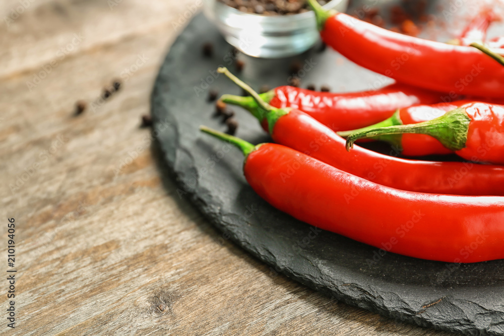 Slate plate with fresh chili peppers on wooden background, closeup Slate plate with fresh chili peppers on wooden background, closeup