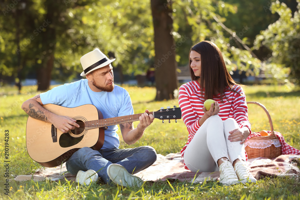 Happy couple with guitar resting on picnic in spring park