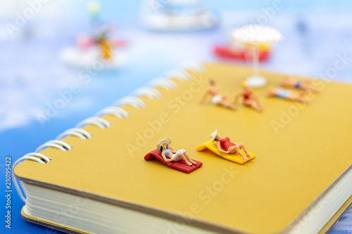 Miniature people: Travelers lie sunbathe on the book brown and blue ocean. Image use for vacation, summer, relax time concept.