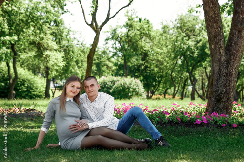 Happy pregnant woman, family couple in the park, green floral background. Young dad gently stroking the belly of his pregnant wife. Future father are touching a pregnant belly of mother. Copy space