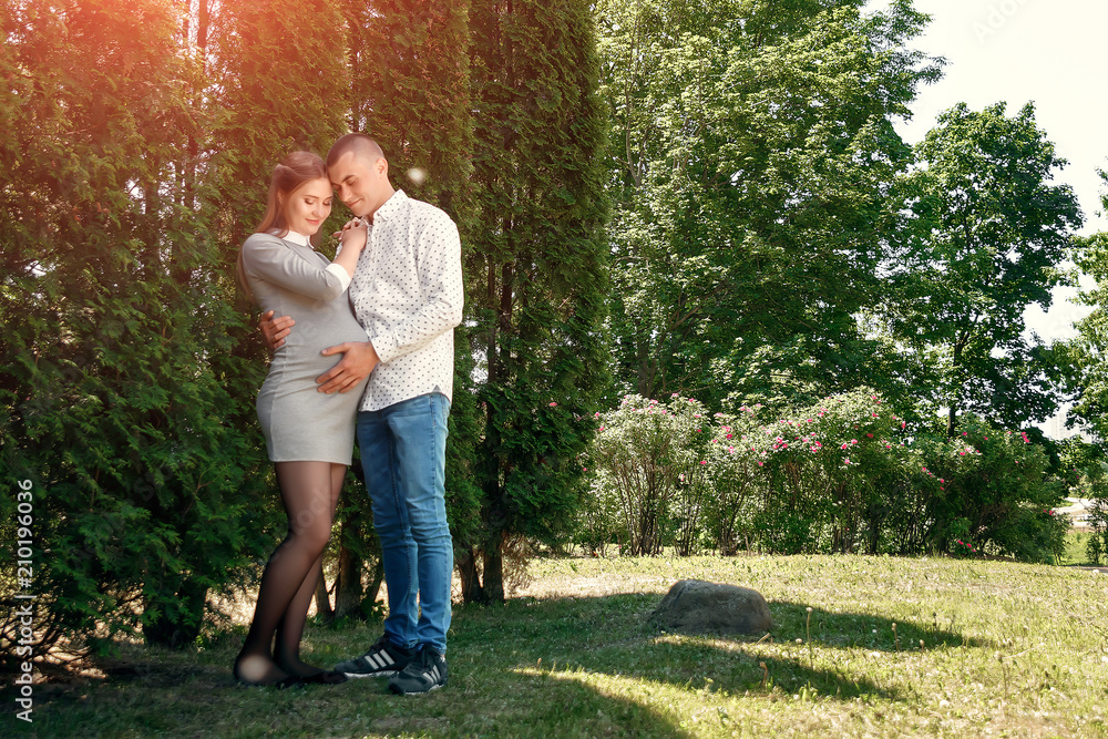 Fototapeta premium Happy pregnant woman, family couple in the park, green floral background. In anticipation of a miracle, a child. Family life, children, pregnancy, family, father, mother. Copy space