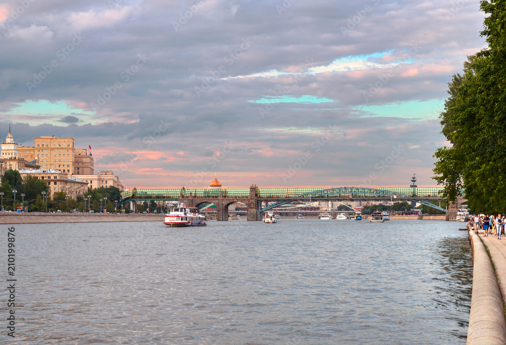 Obraz premium people walk along the Pushkinskaya embankment of Gorky Park against the background of the Moscow River and Andreevsky bridge, Moscow,Russia