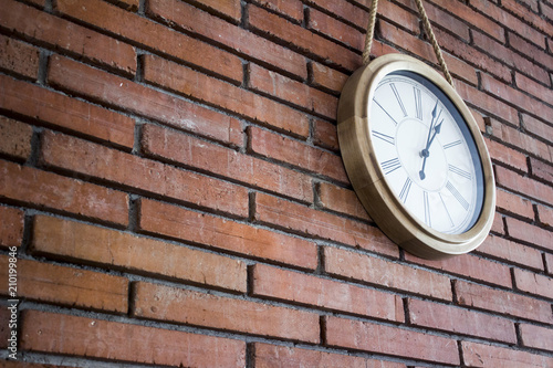 Wallpaper Mural Side medium shot of a wooden classic and simple wall clock hanging in a red brick wall by a rope. It has roman numerals. Canted shot. Torontodigital.ca