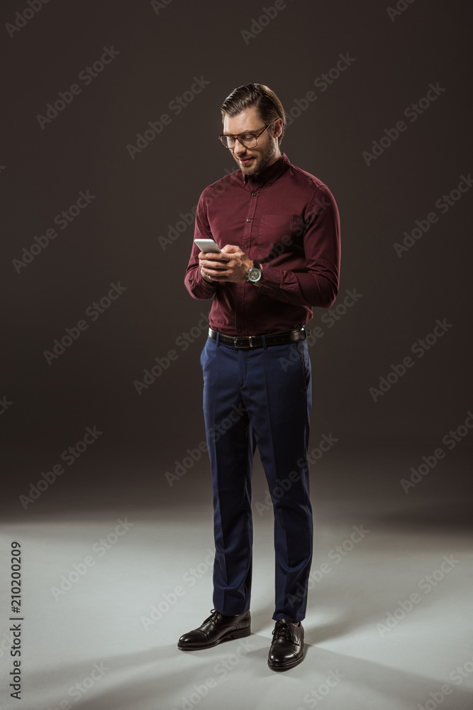 full length view of handsome man in eyeglasses using smartphone on black full length view of handsome man in eyeglasses using smartphone on black
