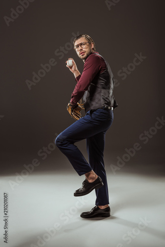 full length view of serious businessman in eyeglasses playing baseball on black