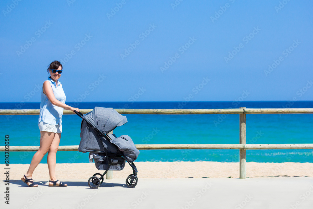 parenting and travel concept side view of young mother pushing baby stroller on the beach Stock Foto Adobe Stock