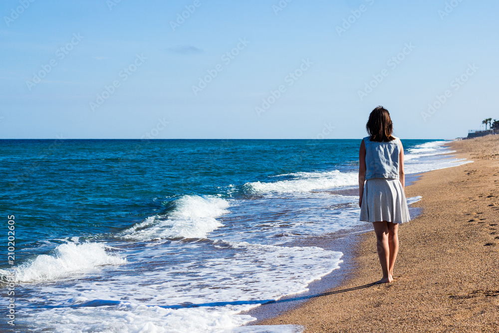 vacation concept  - back view of woman walking on the sunset beach