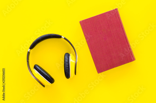 Distance education, e-learning concept. Headphones near hardback book with empty cover on yellow background top view copy space