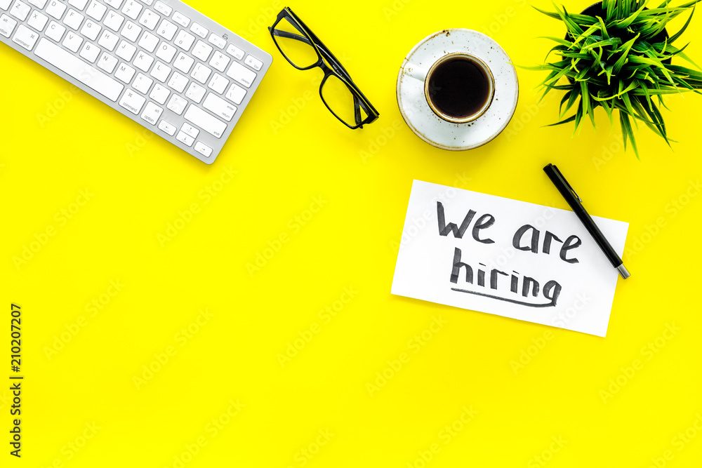 Search for worker, employee concept. We are hiring lettering on work desk on yellow background top view copy space Search for worker, employee concept. We are hiring lettering on work desk on yellow background top view copy space