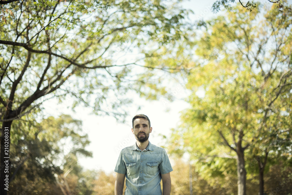 Minimalist portrait of white young man with blue shirt in a natural environment with trees, branches with leaves and a clear blue sky. Natural bucolic image. Minimalist portrait of white young man with blue shirt in a natural environment with trees, branches with leaves and a clear blue sky. Natural bucolic image.