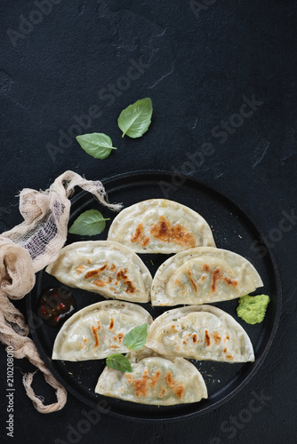 Metal tray with fried potstickers dumplings on a black stone background, vertical shot with copyspace
