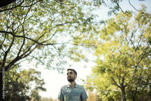 Minimalist portrait of white young man with blue shirt in a natural environment with trees, branches with leaves and a clear blue sky. Natural bucolic image. © josemanuelerre