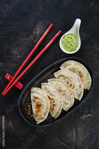 Cast-iron serving pan with fried potstickers, flatlay on a dark brown stone background, vertical shot