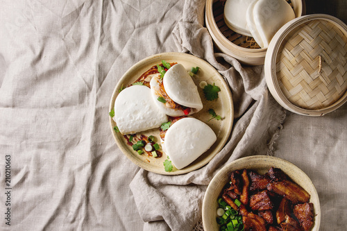 Asian sandwich steamed gua bao buns with pork belly, greens and vegetables served in ceramic plate over linen tablecloth. Asian style fast food dinner. Flat lay, space