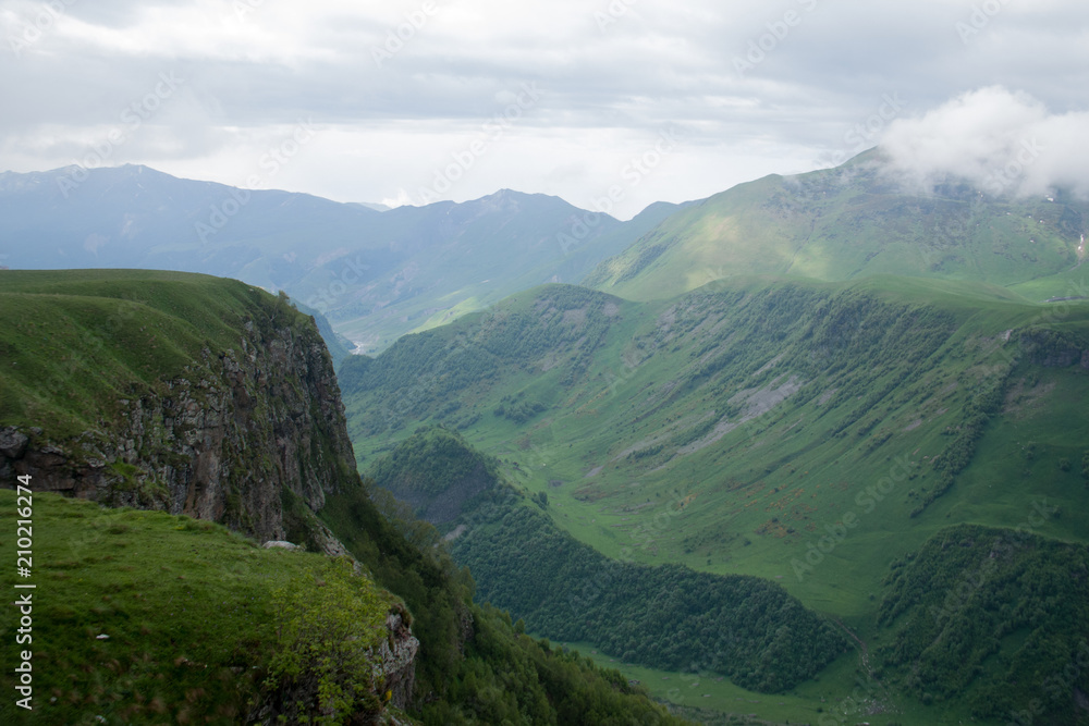 Naklejka premium Georgian green velvet mountains with snow on top in foggy day