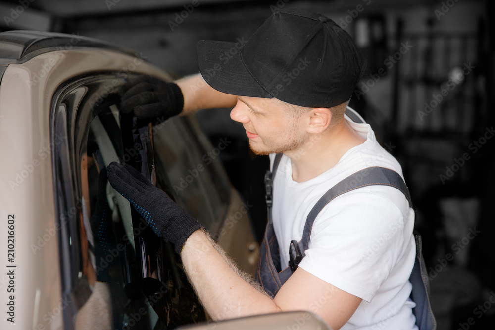 Master installs tint film for car glass with hairdryer and spatula with glare of light. Concept tinting wrapping Master installs tint film for car glass with hairdryer and spatula with glare of light. Concept tinting wrapping