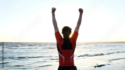 Man raises his hands up and jumps triumphantly at the finish on the background of kitesurfers at sunset