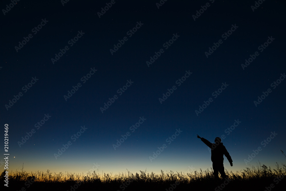 Astronomer points his hand at night the starry sky on a background of a twilight horizon.