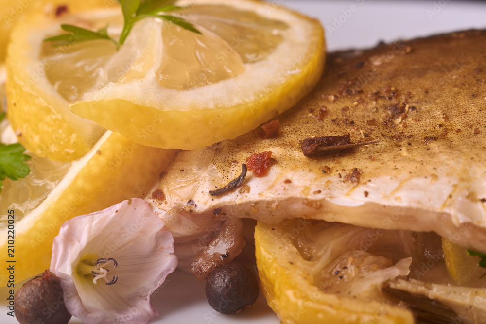 Baked fish with lemon, spices and herbs on white plate on wooden background without head Baked fish with lemon, spices and herbs on white plate on wooden background without head