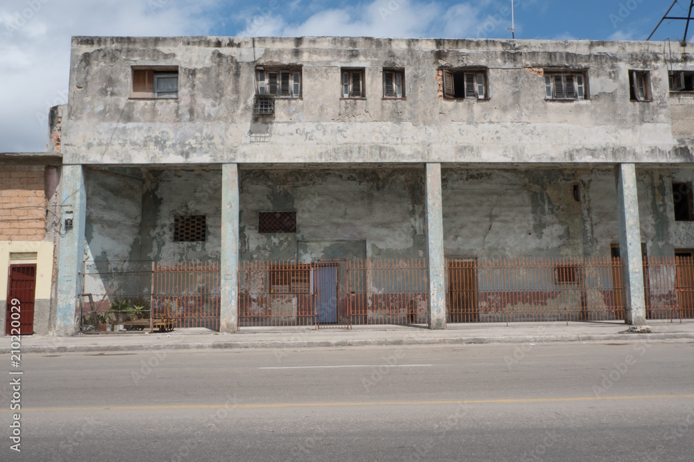Run down concrete building with small apartment on the first floor. Small windows open to let in cool breeze. Old building next to the road in Havana, Cuba.