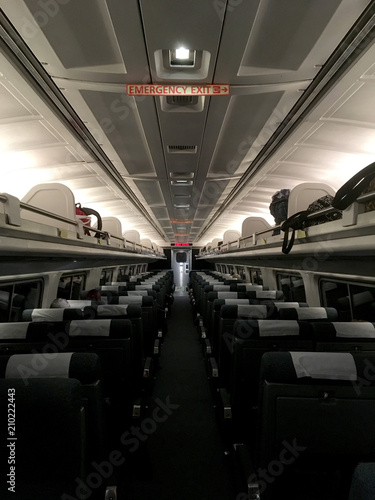 Looking up the aisle of a mostly empty plane in economy class. Illuminated emergency exit sign inside a plane. Backs of seats of a large commercial airline jet before take off. Empty airplane.