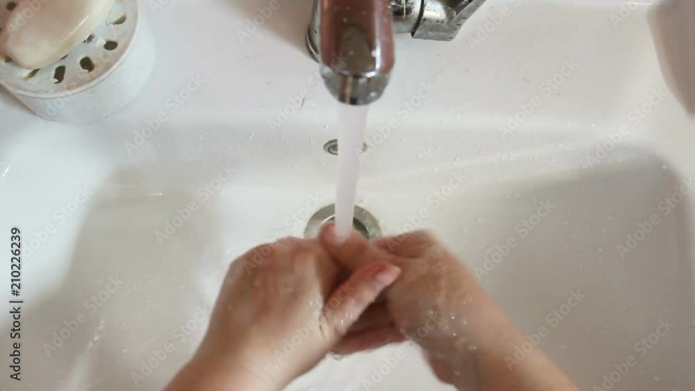 Washing of hands with soap under running water.Female hands under a stream of water against a white shell. top wiev, close up. Then she rubs her hands with a striped towel Washing of hands with soap under running water.Female hands under a stream of water against a white shell. top wiev, close up. Then she rubs her hands with a striped towel