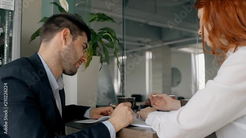 Two collegaues are working together on the project in the office: man in suit making notes and woman with red hair talking to him. Indoors. photo