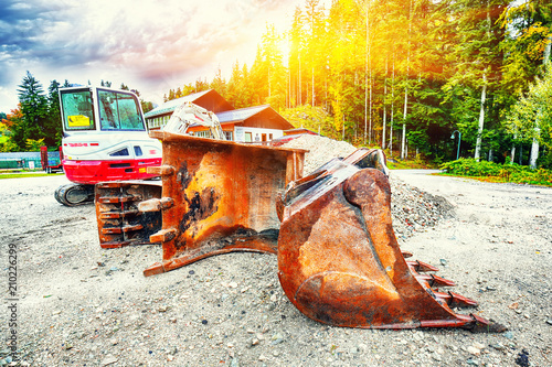 Fotografi Excavator in summer day in forest against background of trees.