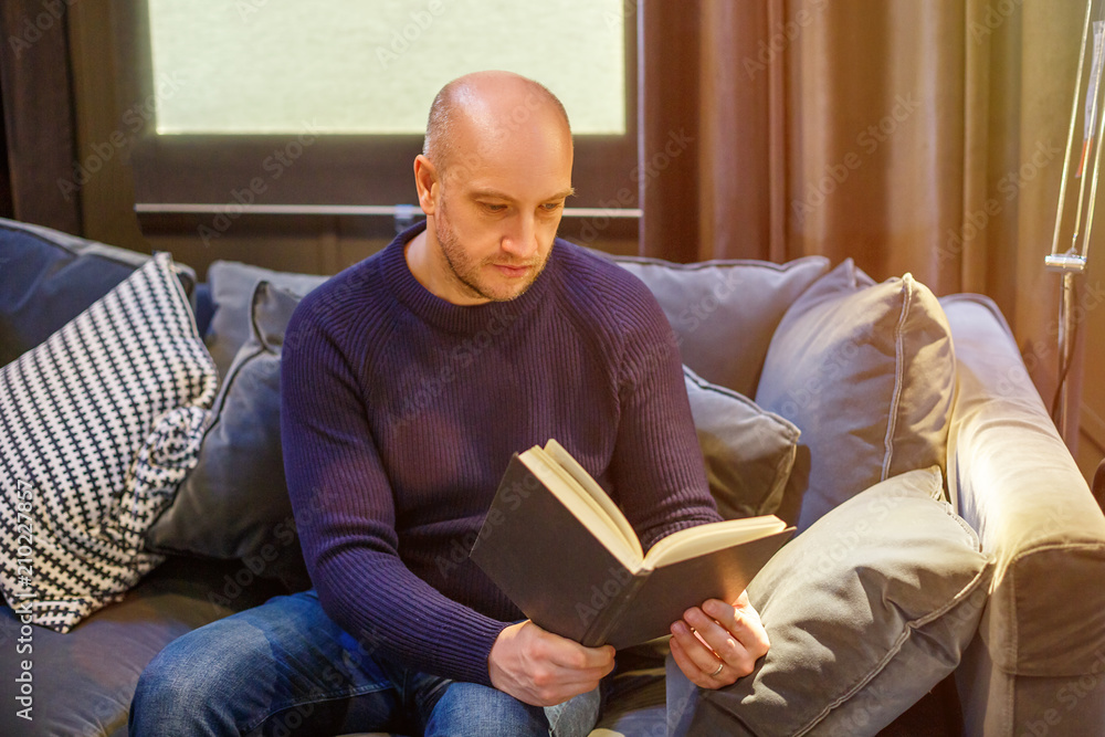 adult man sitting on the couch and reading a book