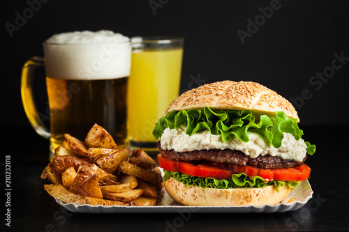 Italian version of a classic American hamburger with a meatball, fresh tomatoes and lettuce leaves and parmesan cheese sauce. European street food and beer