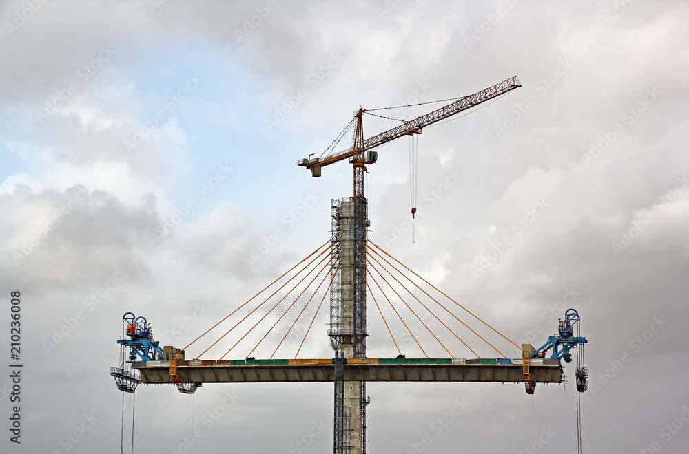 Naklejka premium Erecting cable stayed bridge progressing on two sides of the tall central concrete pier using tower crane for the third bridge over Mandovi River in Goa, India
