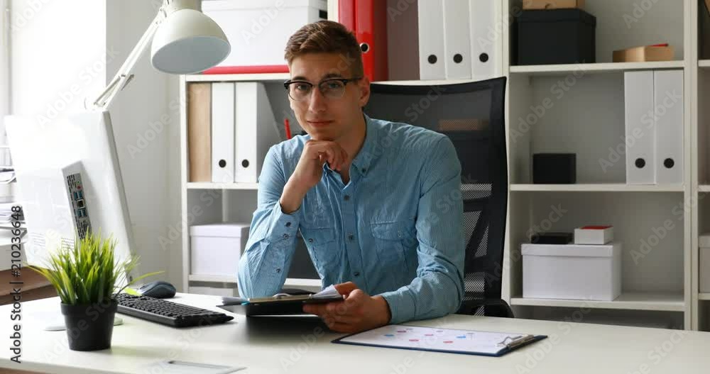 office worker wearing glasses, sitting at table and looking at camera office worker wearing glasses, sitting at table and looking at camera