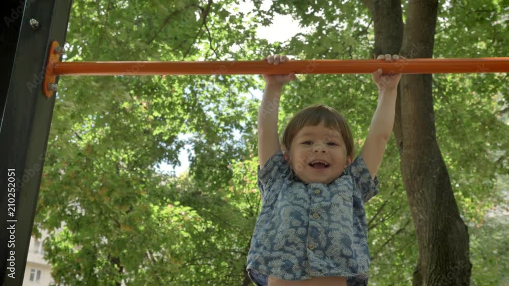 Young father helping his little son to do pull-ups, dad training son in park, smiling Young father helping his little son to do pull-ups, dad training son in park, smiling