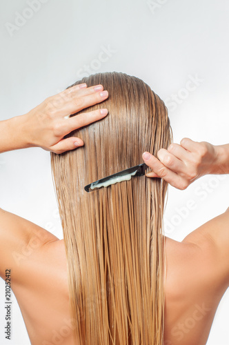 Blond woman with long wet hair is applying hair conditioner photo