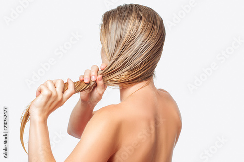 Blond woman with long wet hair is applying hair conditioner