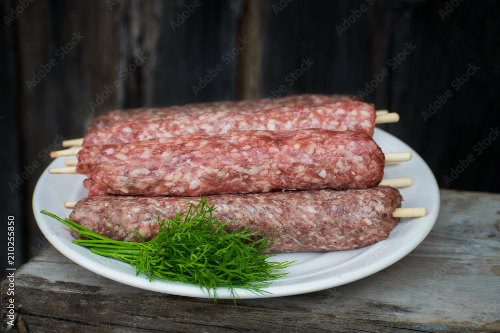 Raw lulya kebab from meat on a white plate and wooden board with with dill.