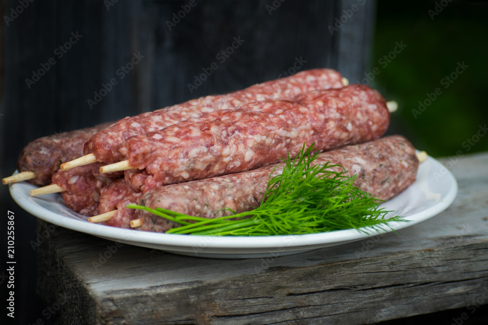 Fototapeta premium Raw lulya kebab from meat on a white plate and wooden board with with dill.