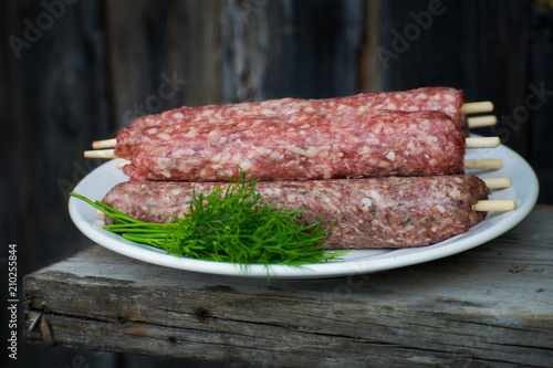 Raw lulya kebab from meat on a white plate and wooden board with with dill. photo