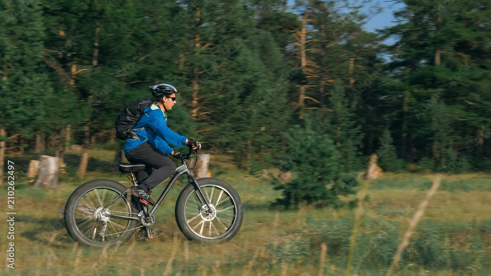 Obraz premium Fat bike also called fatbike or fat-tire bike in summer riding in the forest. The guy rides a bicycle among trees and stumps. He overcomes some obstacles on a bumpy road.