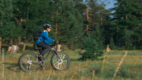 Fat bike also called fatbike or fat-tire bike in summer riding in the forest. The guy rides a bicycle among trees and stumps. He overcomes some obstacles on a bumpy road.