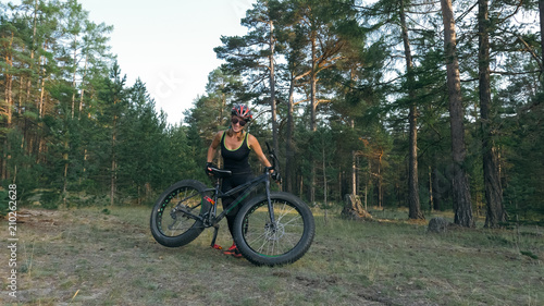 Fat bike also called fatbike or fat-tire bike in summer riding in the forest. Beautiful girl and her bicycle in the forest. She rolls her bike and poses to the operator.